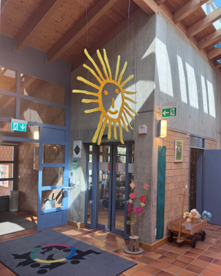 Eingang zum Lädeli mit dem Schmutzfänger Teppich, der das Logo der Stiftung MBF zeigt und einer grossen Sonne aus Holz die von der Decke herunterhängt.
