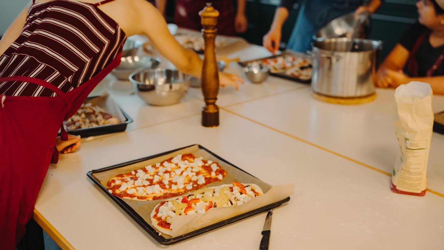 Gruppe backt zusammen Pizza. Gemeinsames Kochen in der Schule – Teamarbeit, Selbstständigkeit und Freude am Lernen in der Küche.