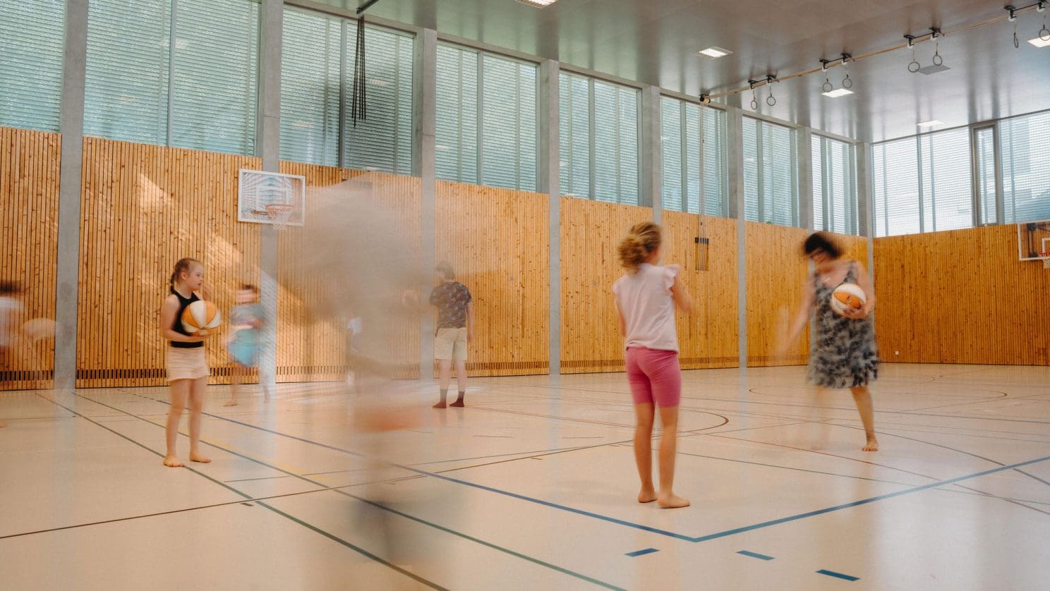 Kinder spielen Basketball in der Turnhalle - Spass und Motorik an der HPS