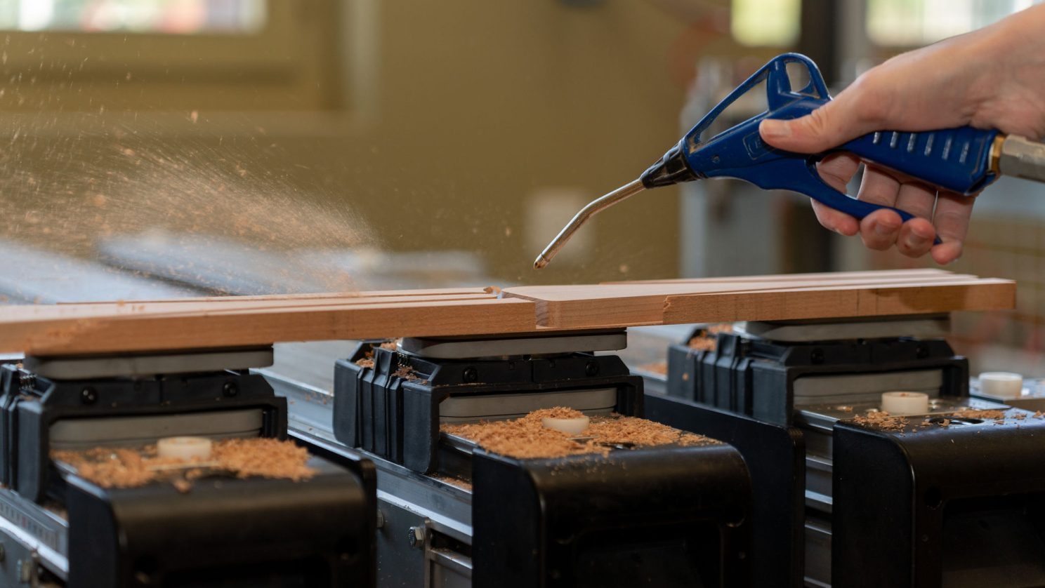 Hand bläst Holzspäne mit Druckluftpistole weg – Werkstattarbeit bei der Stiftung MBF STEIN MADE.