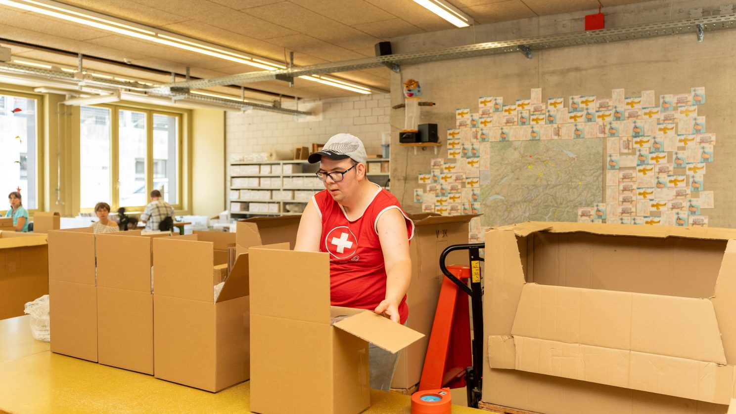 Mitarbeitender mit Unterstützungsbedarf faltet Kartons in der Verpackungsabteilung der Stiftung MBF.