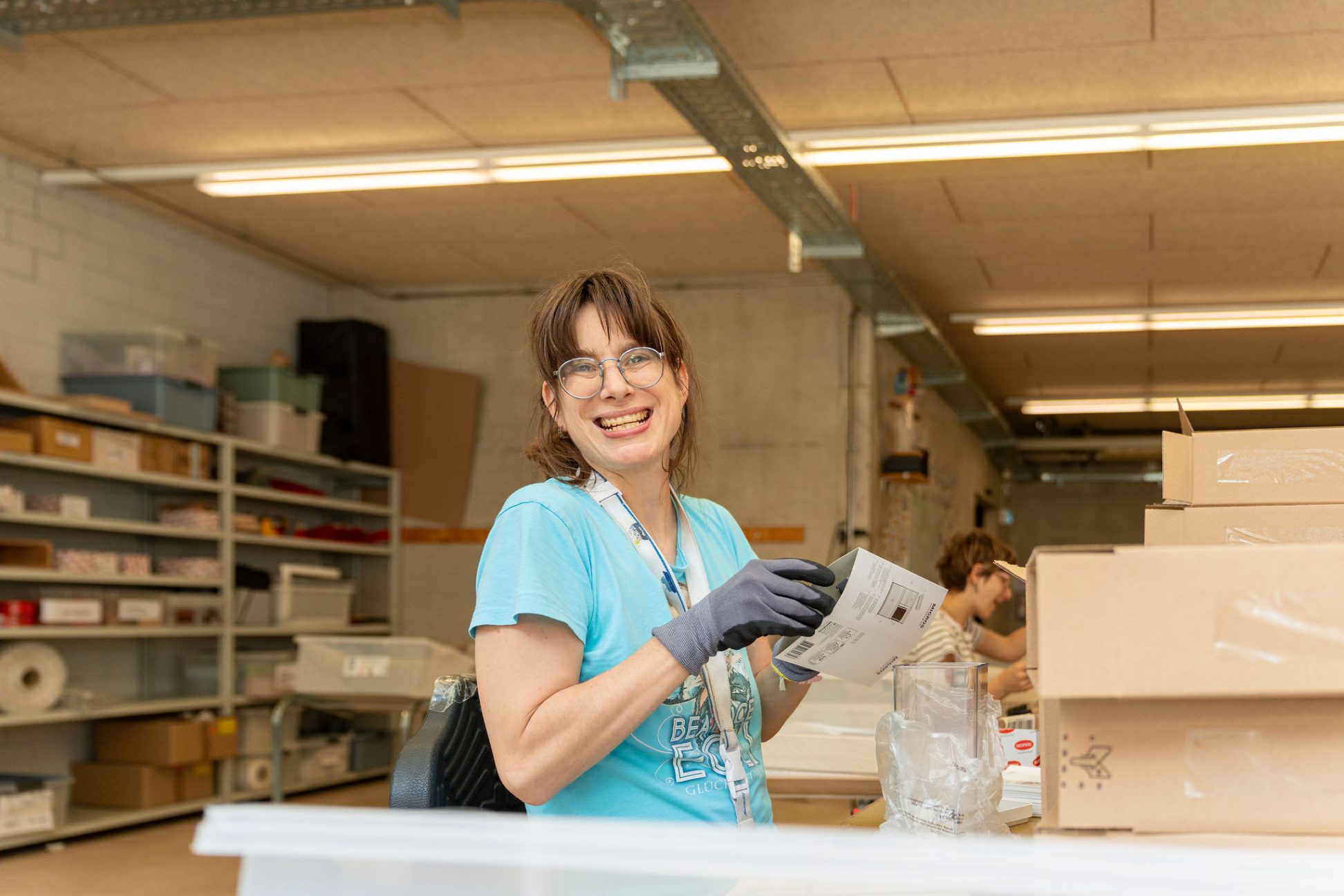 Lächelnde Frau mit Unterstützungsbedarf beim Verpacken in der Werkstatt – Teilhabe und Arbeitsalltag bei der MBF.