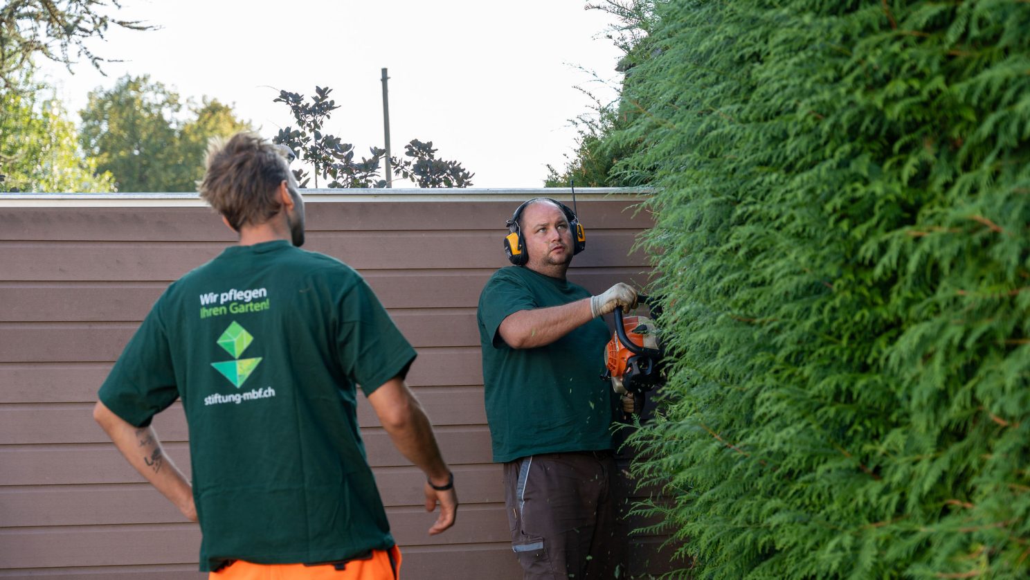 Garten- und Landschaftsteam der Stiftung MBF beim Schneiden einer grünen Hecke.
