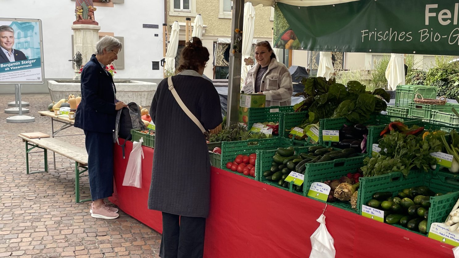 Kundinnen kaufen frisches Bio-Gemüse am Feldhof-Marktstand der Stiftung MBF – Teilhabe und nachhaltige Landwirtschaft.