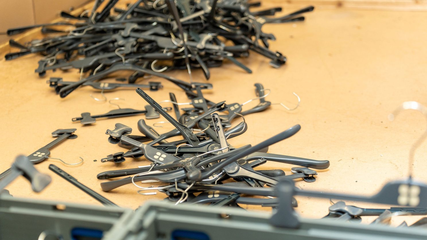 Mehrere schwarze Kunststoff-Kleiderbügel liegen ungeordnet auf einem Arbeitstisch bereit zur weiteren Verarbeitung.