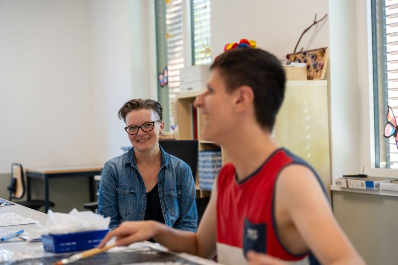 Frau und junger Mann sitzen im Atelier zusammen und lachen - Spass bei der Arbeit in der MBF.