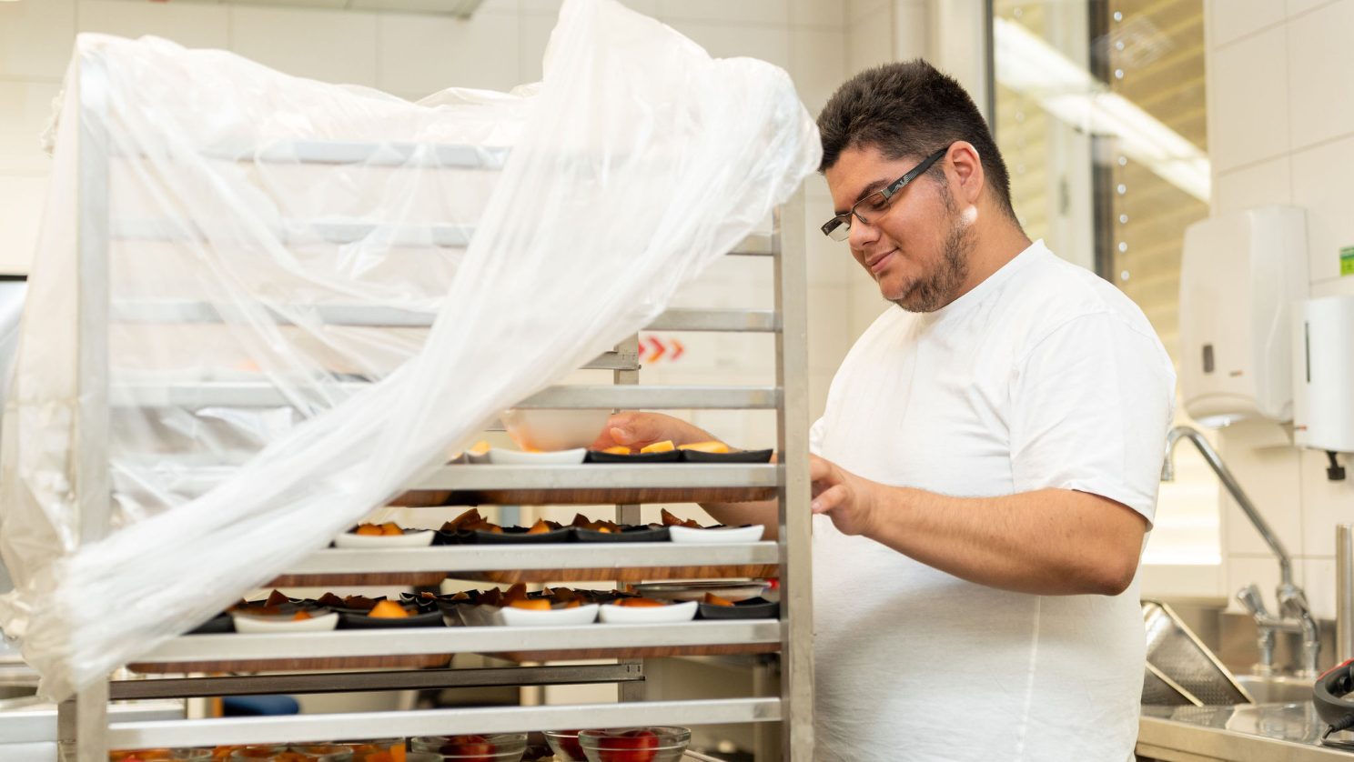 Mitarbeiter sortiert Obstschalen in einem Rollwagen in der MBF Küche.